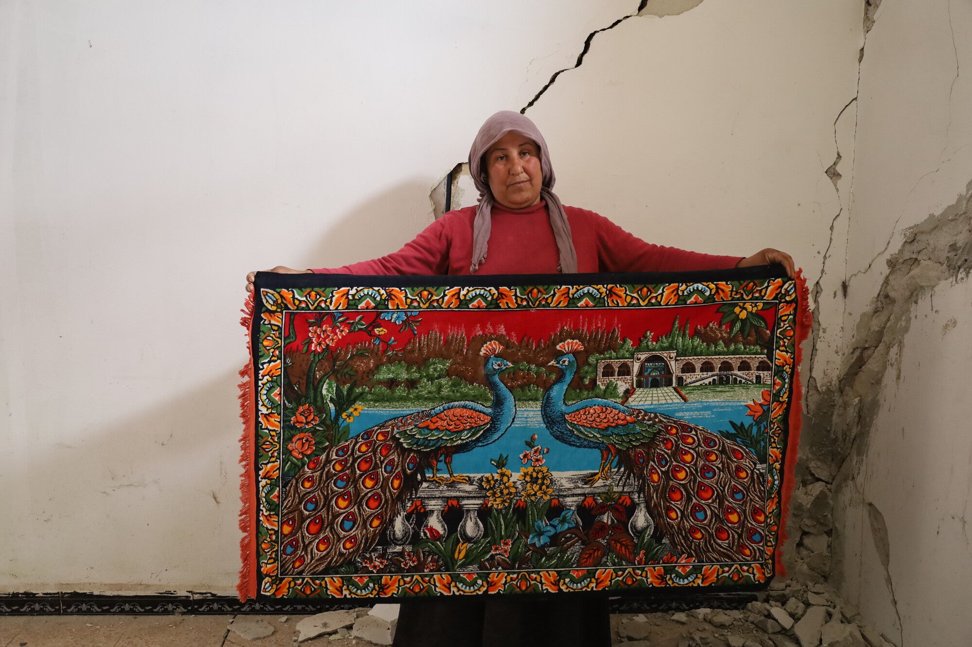 Woman holding a woven rug with a peacock design..