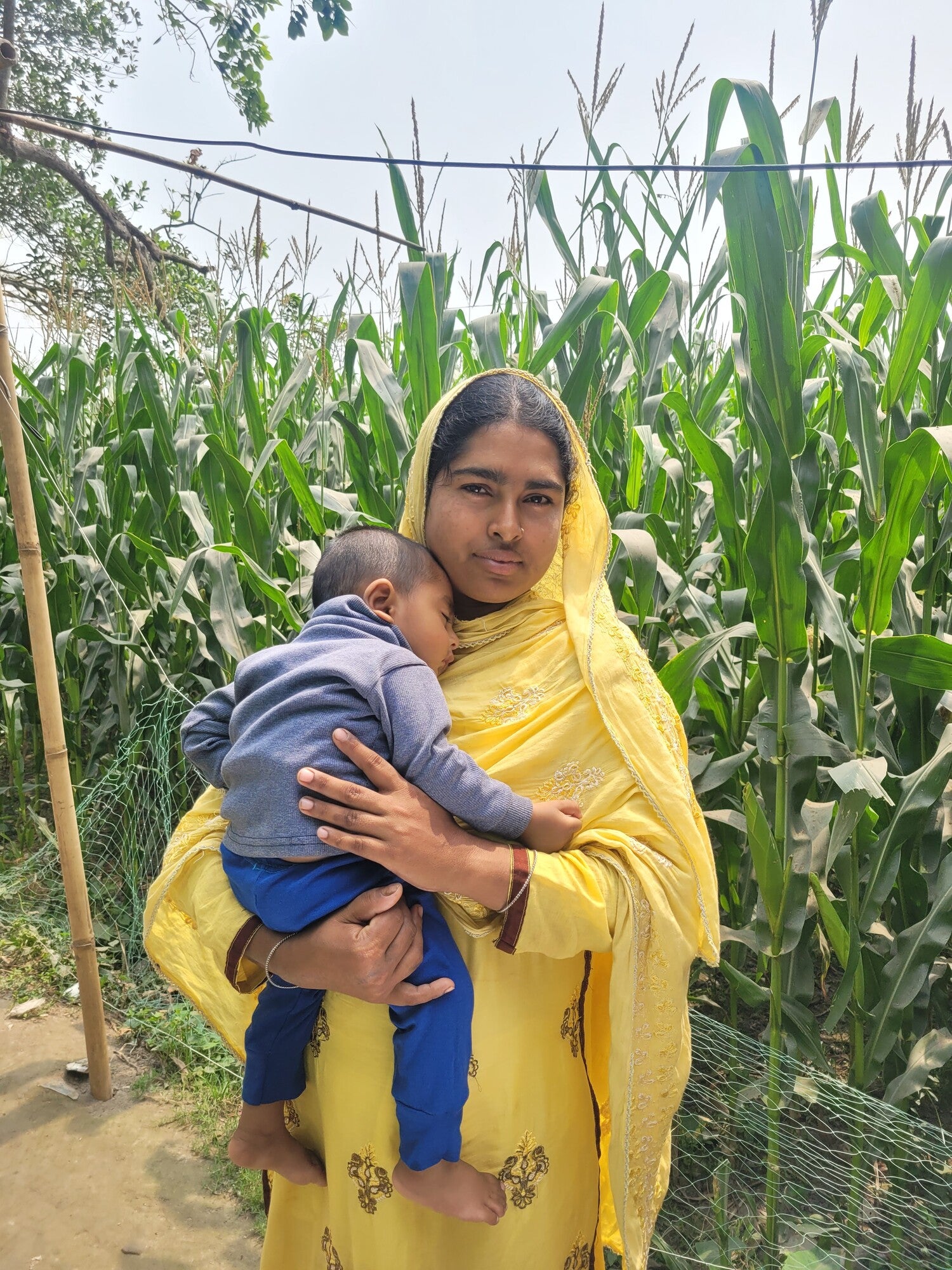 Woman holding a small boy in front of a corn field.