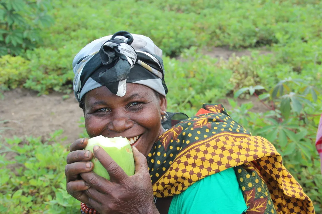 A woman smiles while eating a bright green fruit.