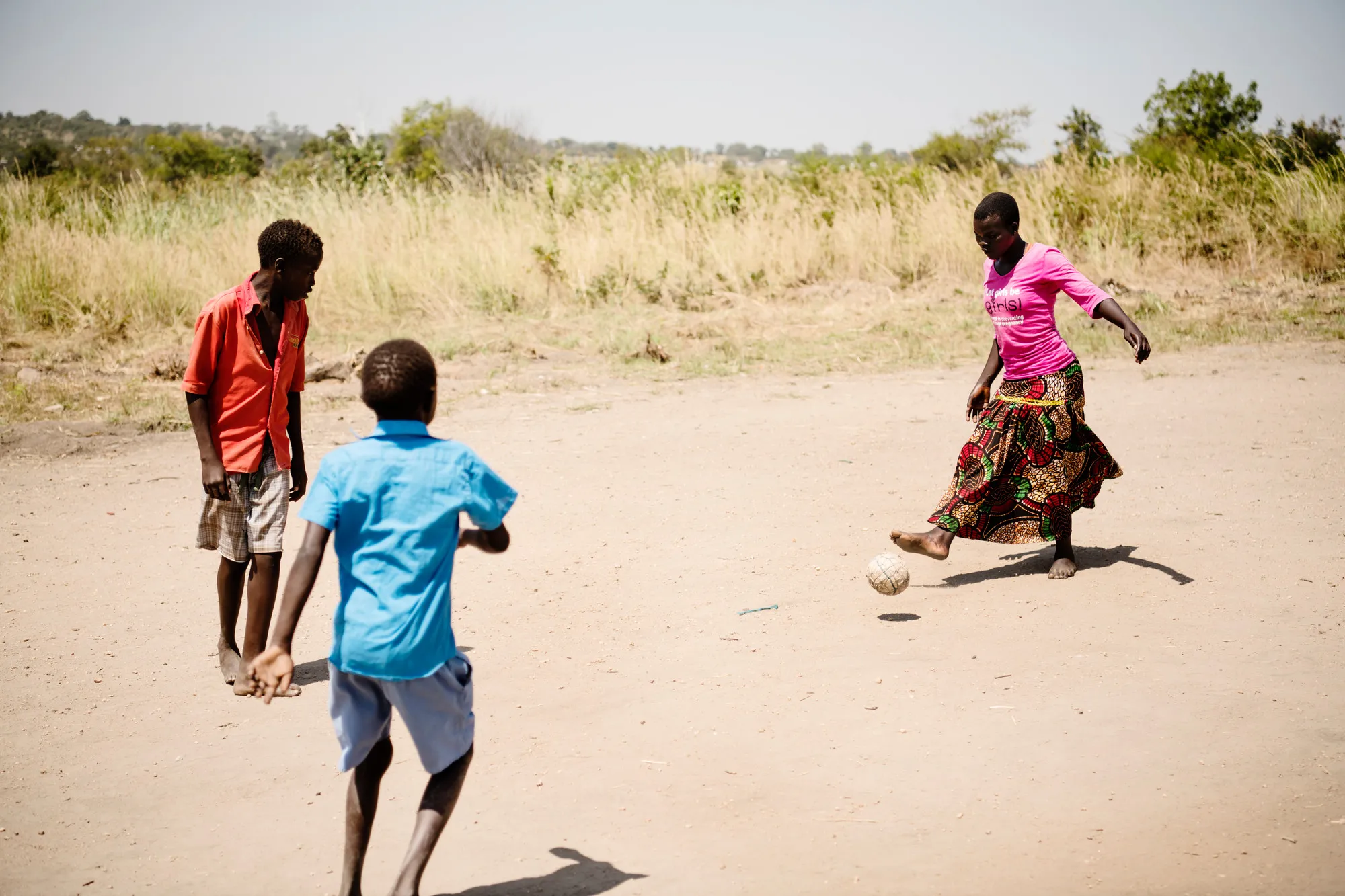 Girl playing soccer on a dirt field with two boys