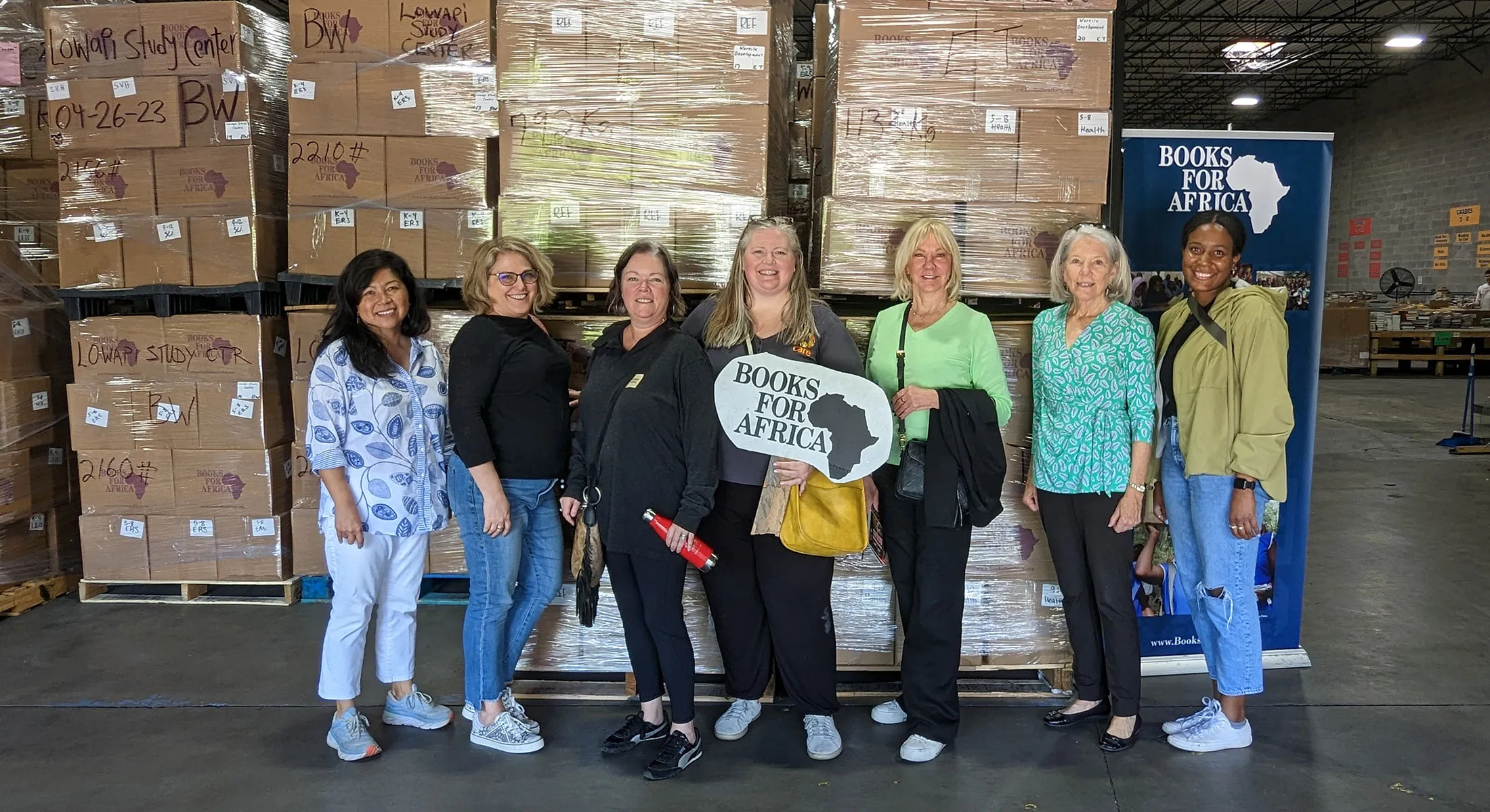 CARE staff and network members posing in front of large stacks of books to be donated abroad.