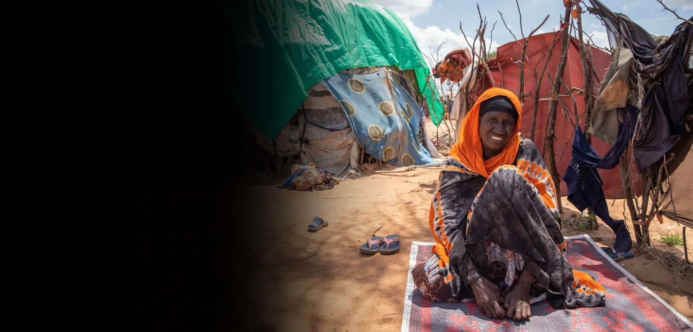 A woman sits on the ground near a makeshift tent.