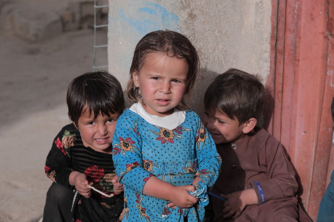 Tres niños afganos se sientan juntos y se apoyan en una casa.