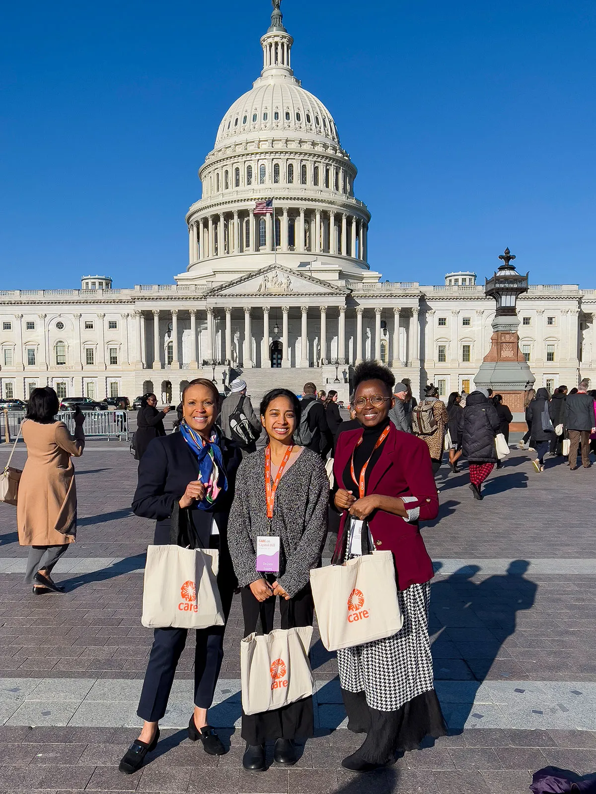 Tres mujeres sonríen frente al Capitolio de Estados Unidos. Cada uno de ellos lleva insignias de CARE y sostiene bolsas de mano de CARE.