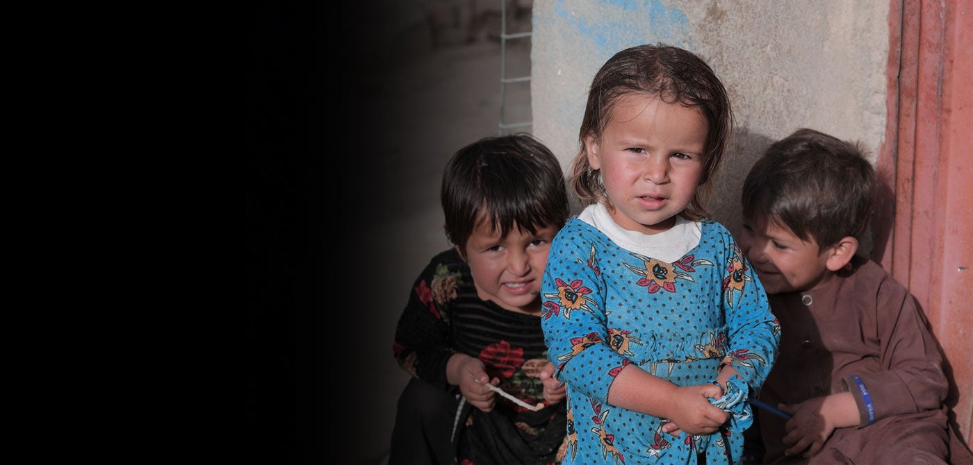Tres niños afganos se sientan juntos y se apoyan en una casa.