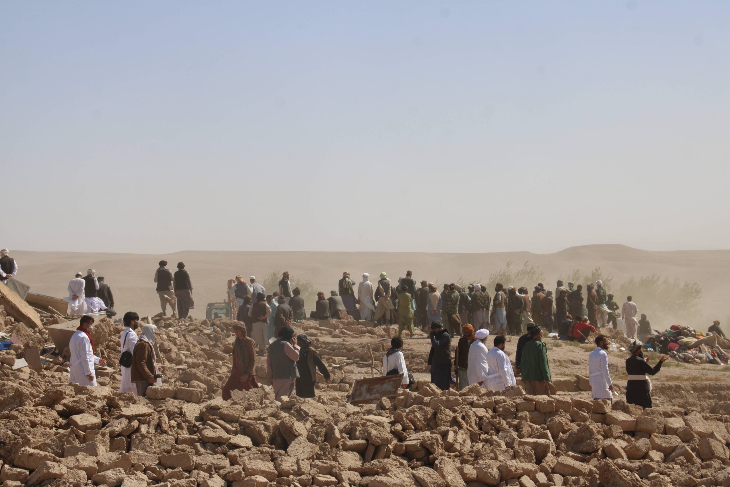 People in Afghanistan stand around rubble after an earthquake.