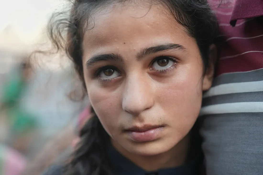 A young Palestinian woman looks off to the side. She is being held by someone out of frame.