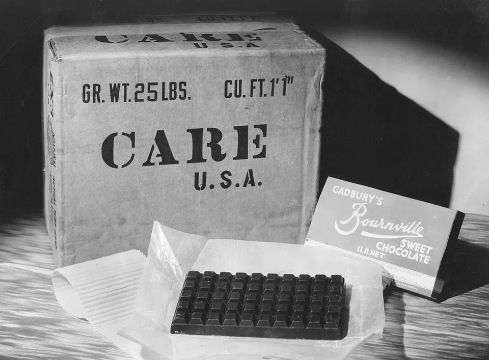 A photo of one of the original CARE Packages from 1948. In front of the box is a large bar of chocolate.