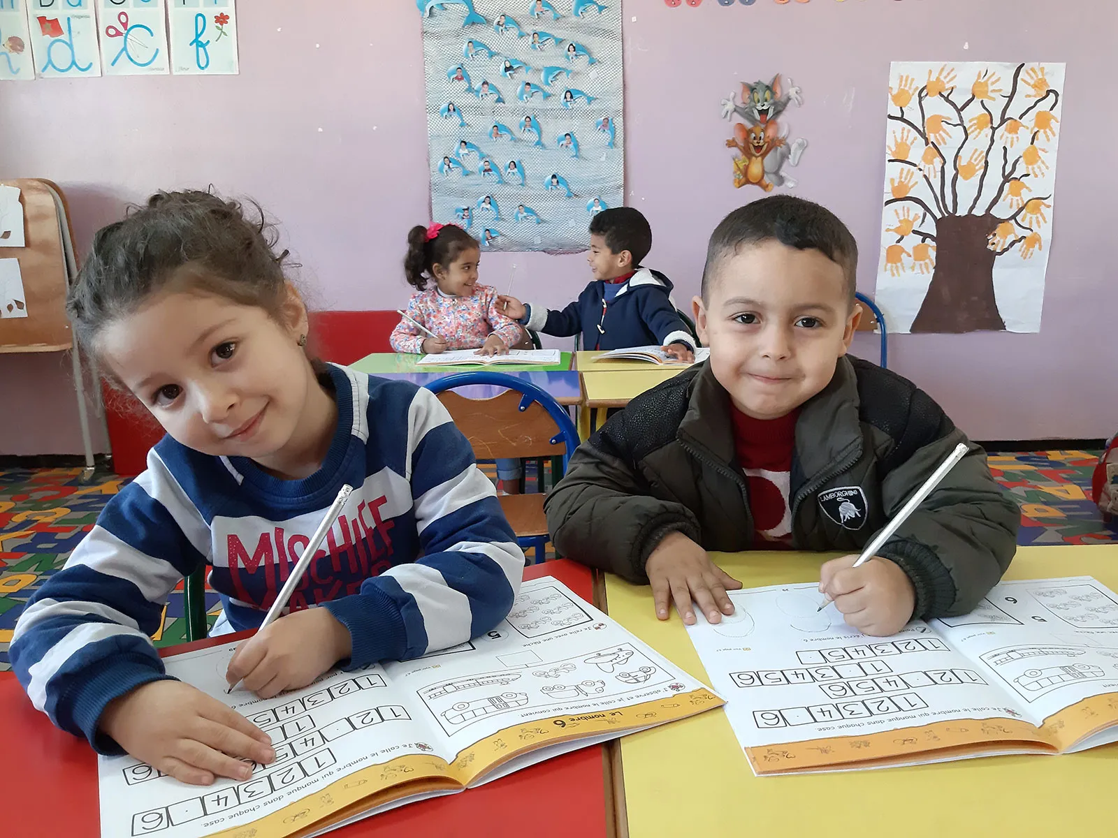 A young Moroccan boy and girl sit together at a desk and fill out worksheets.