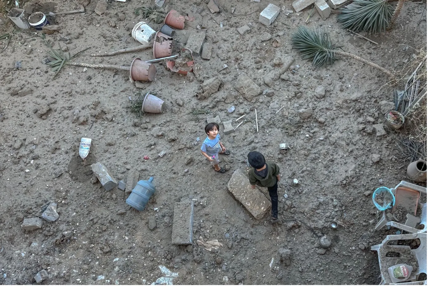 Overhead shot of boy staring up from the middle of a dirt field, another unidentified person walking nearby