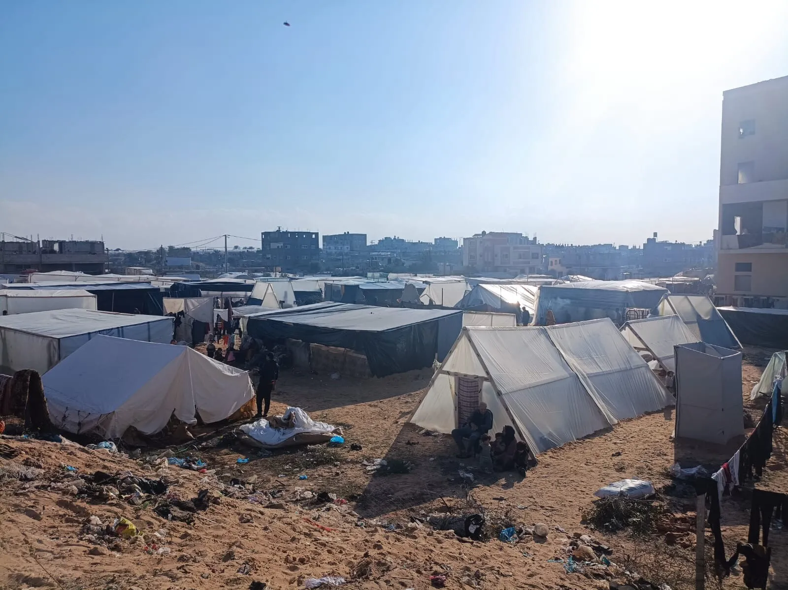 Photo of tents pitched atop dirt in an urban landscape under clear skies