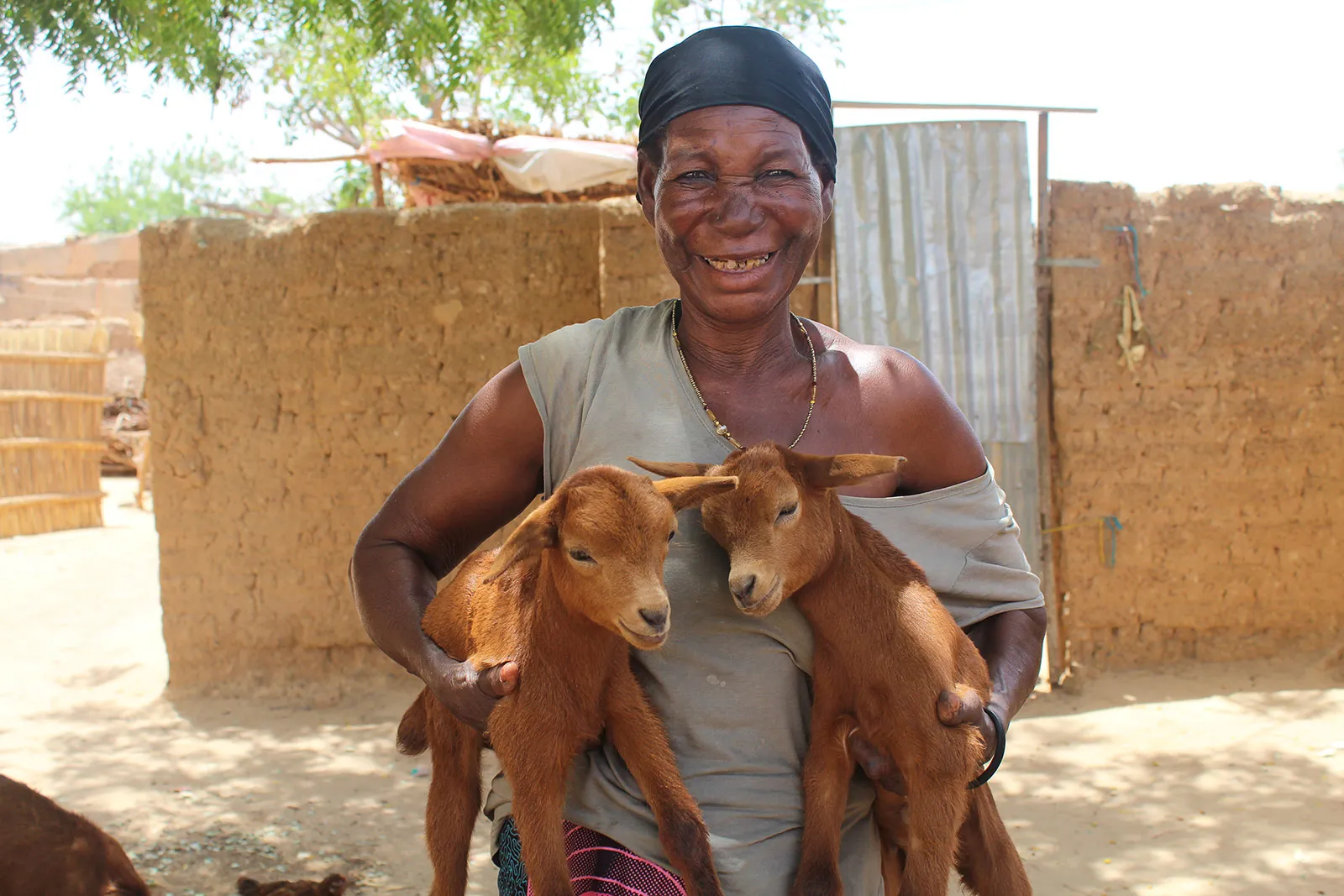 A woman smiles while holding two brown baby goats.