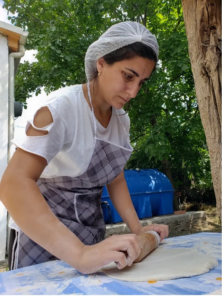 Portrait of woman with white head covering rolling dough with a rolling pin on an outdoor table