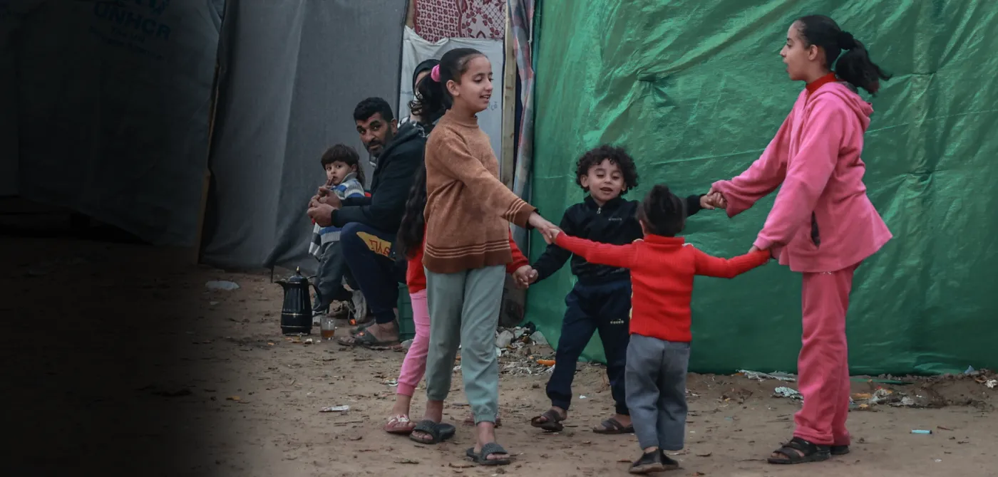 A group of children hold hands in a circle in a camp in Gaza.
