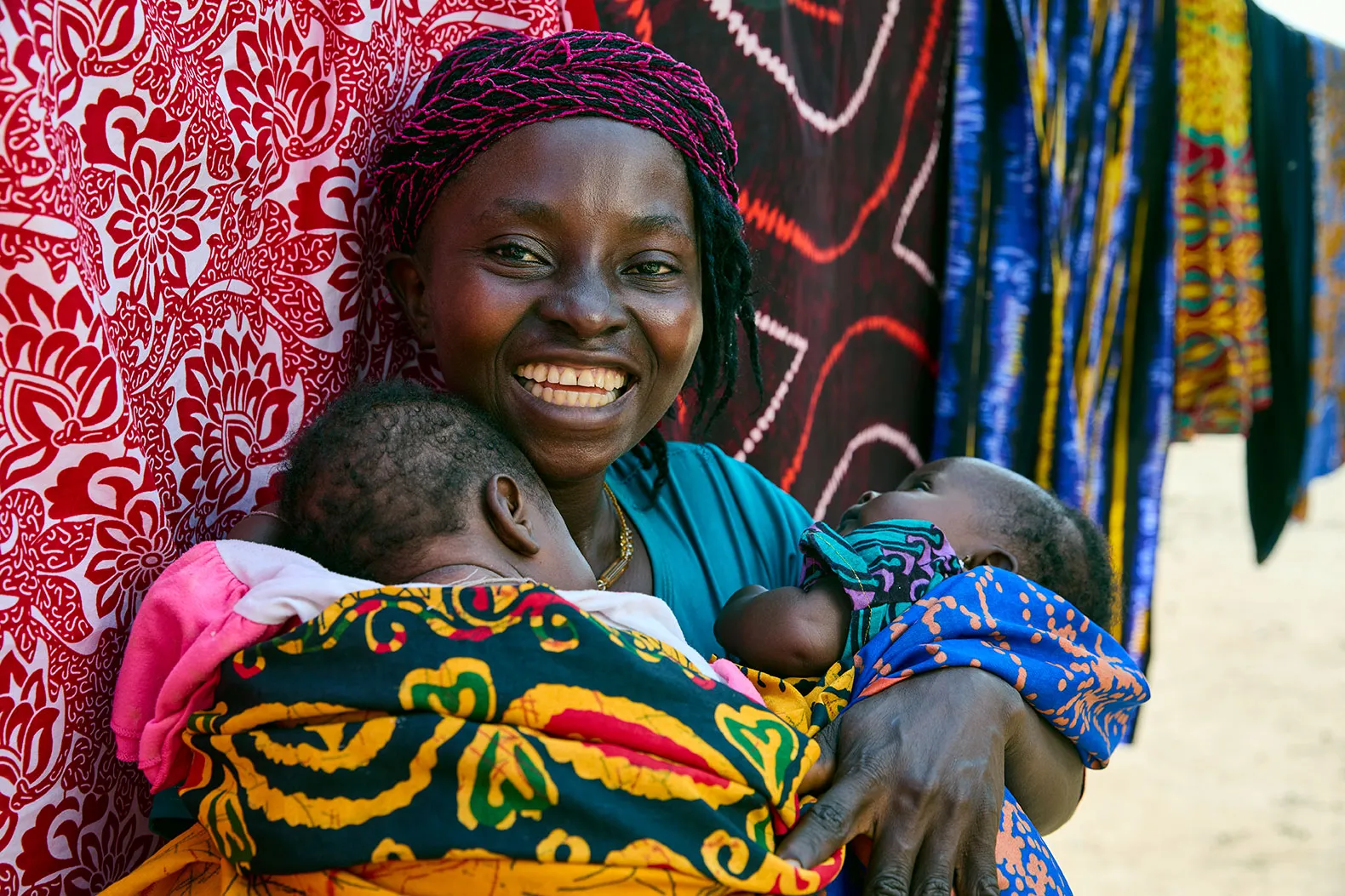 Uma mulher sorri enquanto segura dois bebês perto do peito.