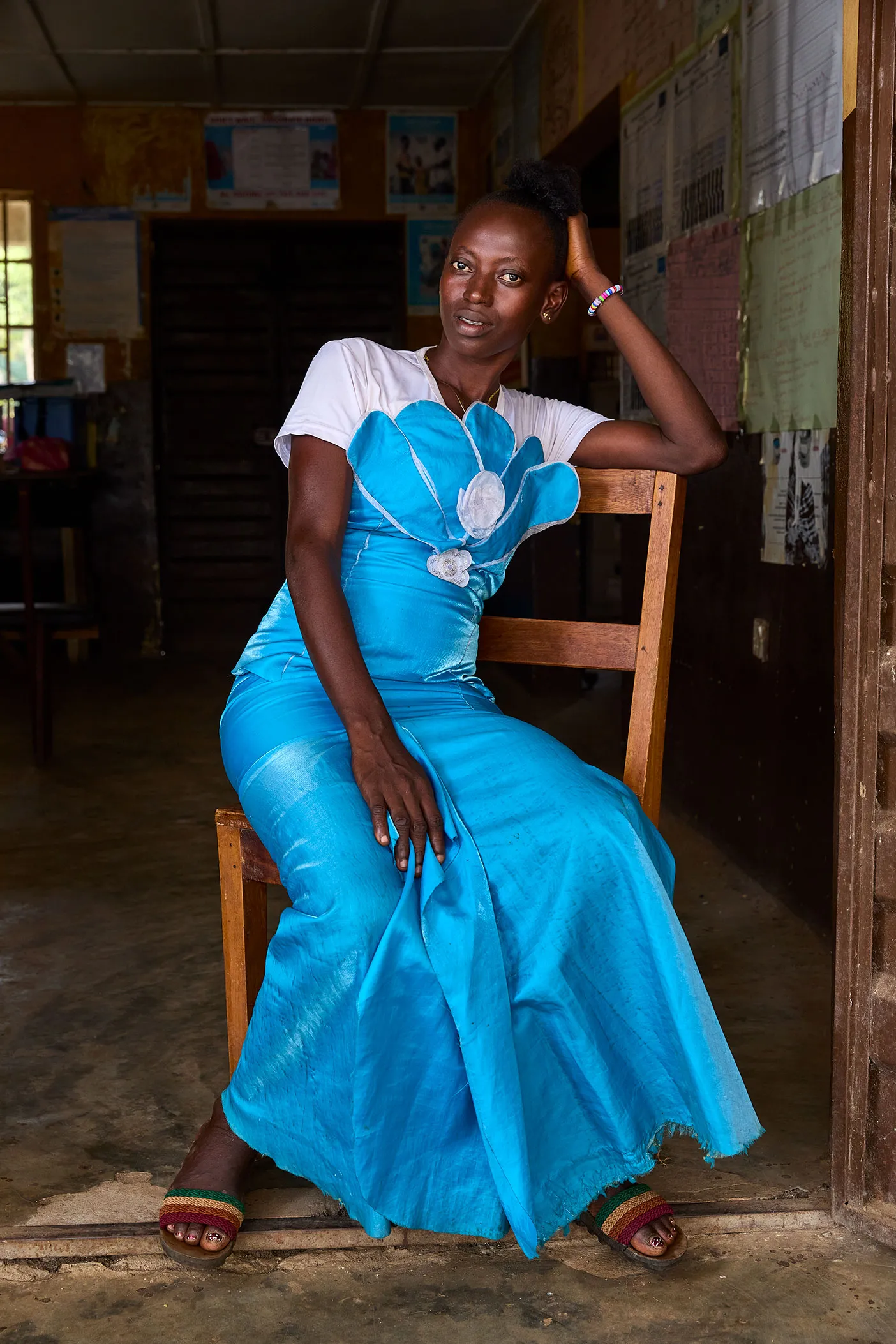 Uma mulher com um vestido longo azul está sentada em uma cadeira de madeira.