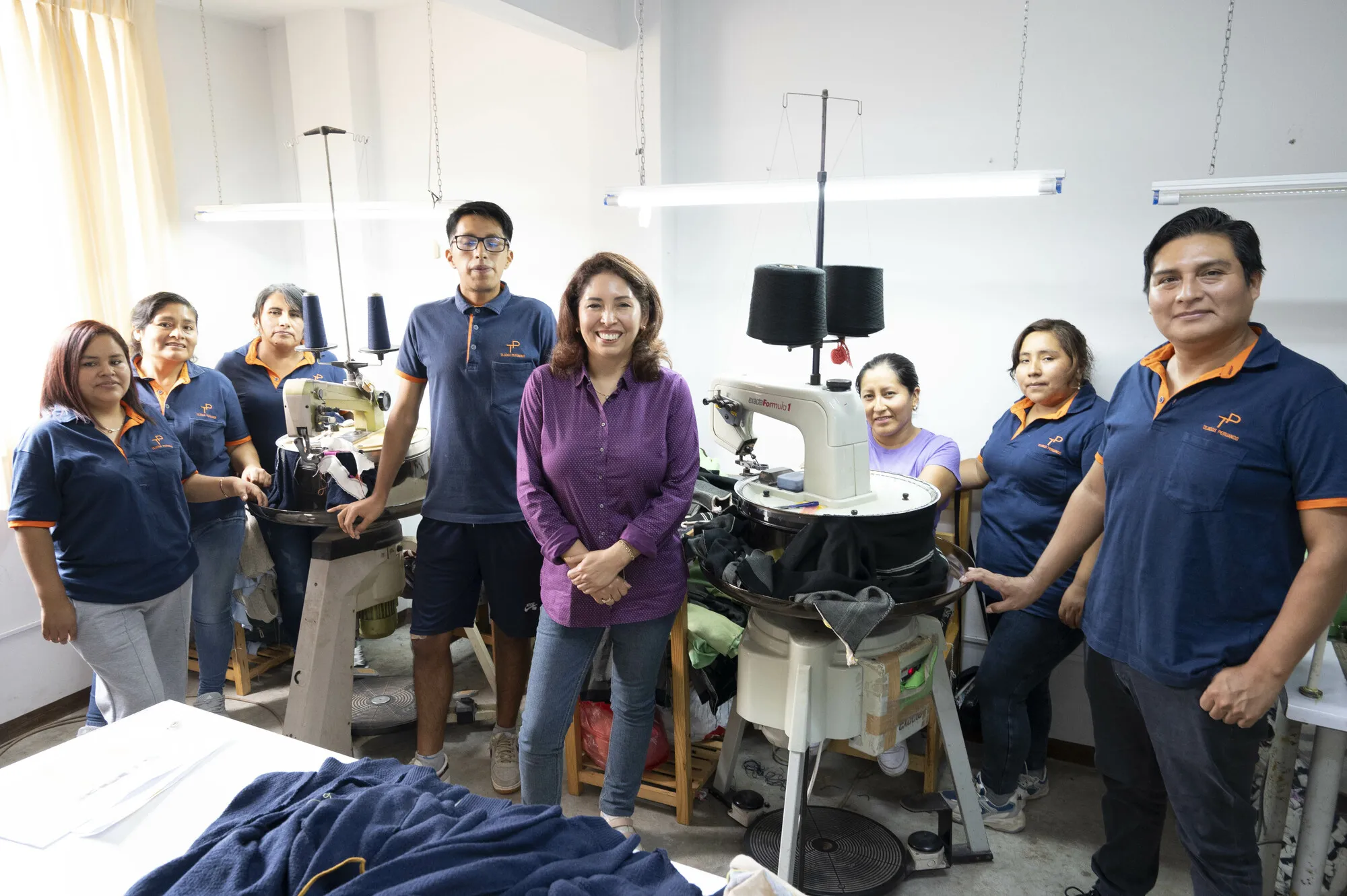 Violeta Mejia surrounded by her employees in an indoor workshop space.