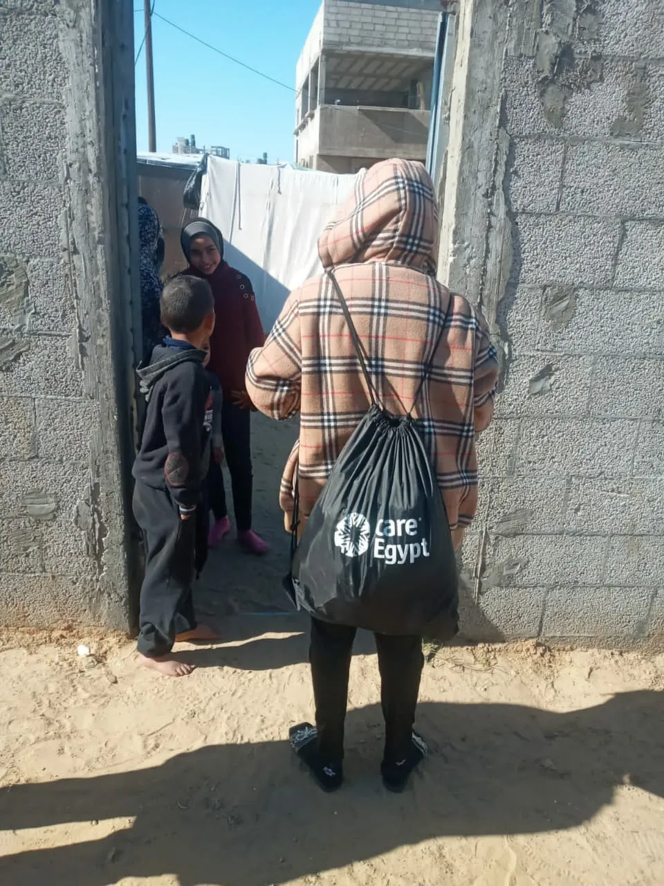 Child, back to camera, carries a bag marked “CARE Egypt,” and talks to other children.