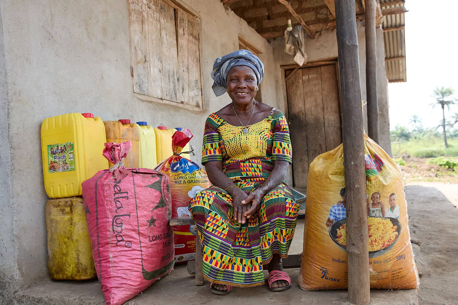 A woman sits outside surrounded by bags of rice.