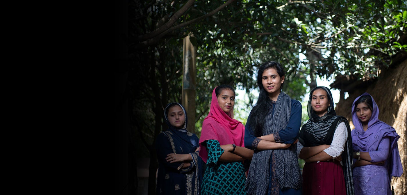 A group of five Bangladeshi girls stand together with their arms crossed.