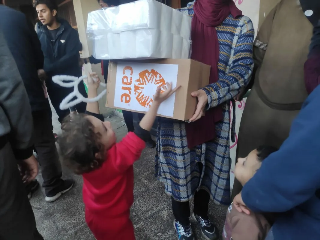 A small child reaches up to their mother, who is holding a CARE aid box.