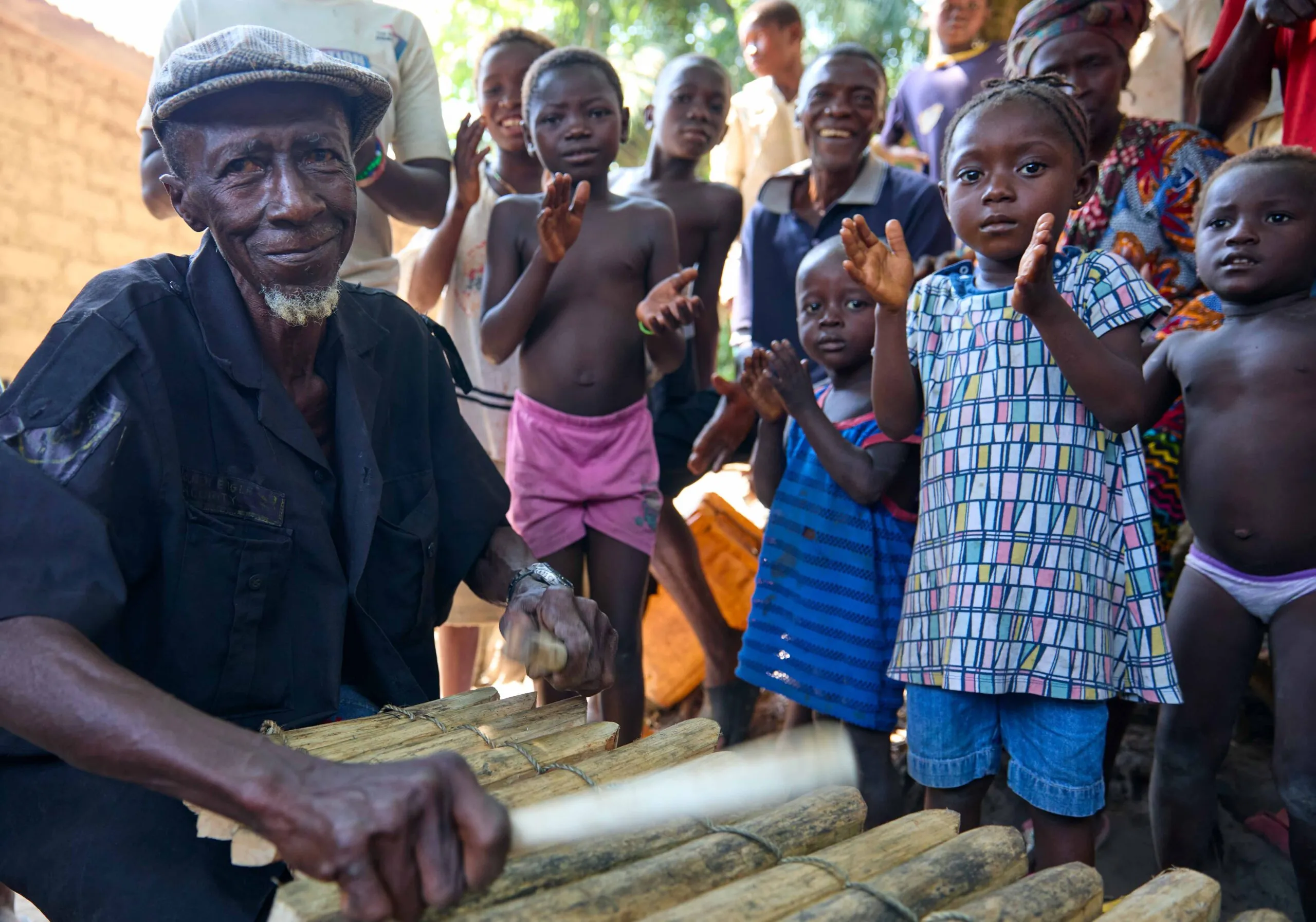Photo of a man playing a marimba while children watch and clap.