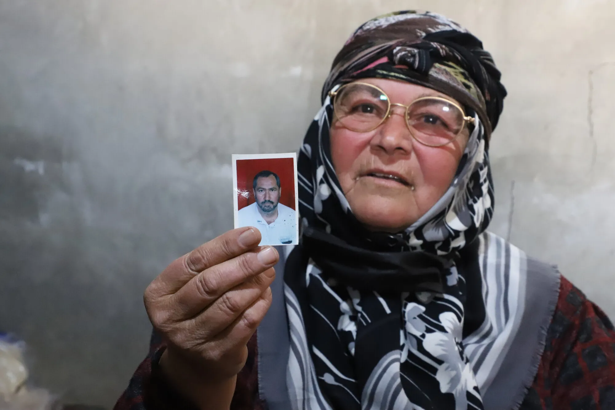 A Syrian woman 's portrait who's holding her late husband's photo.