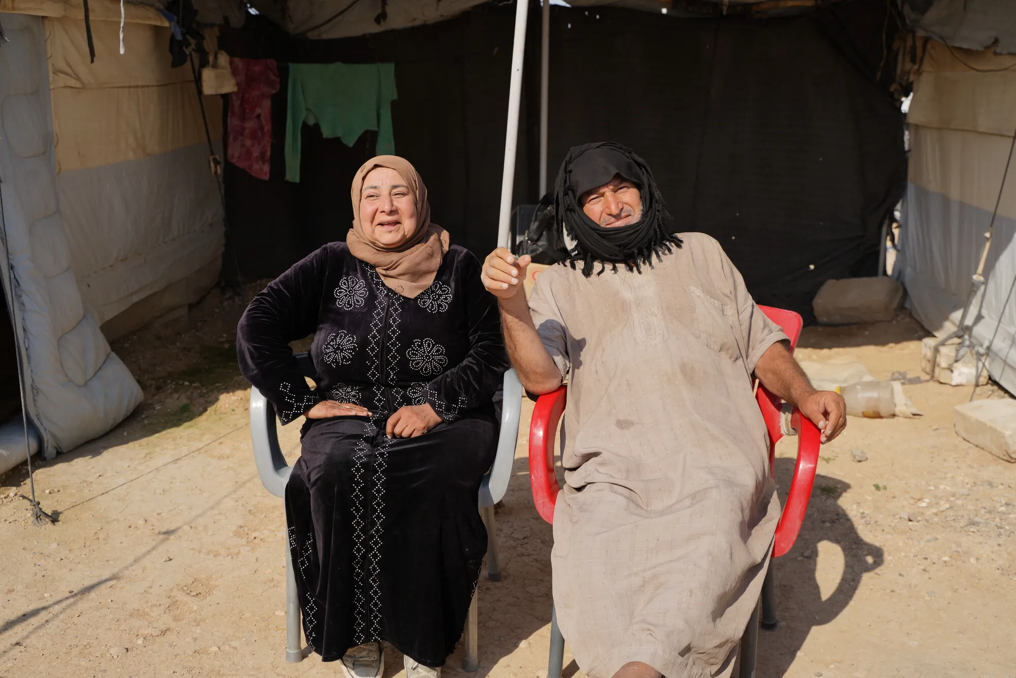 An internally displaced Syrian woman and her husband, sitting next to each other in front of their tent.