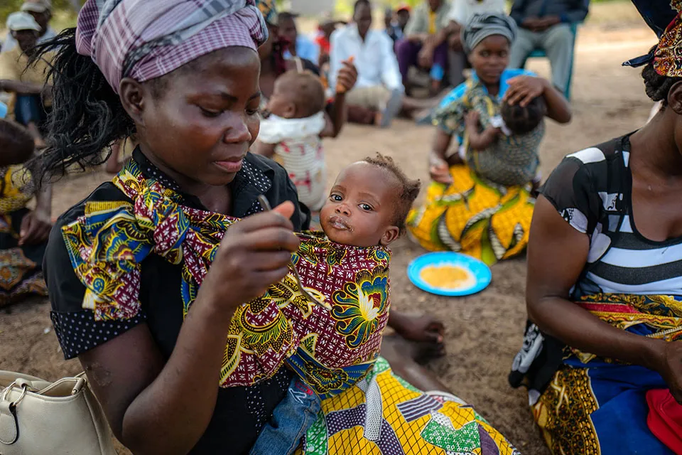 A woman feeds a young child with a spoon.