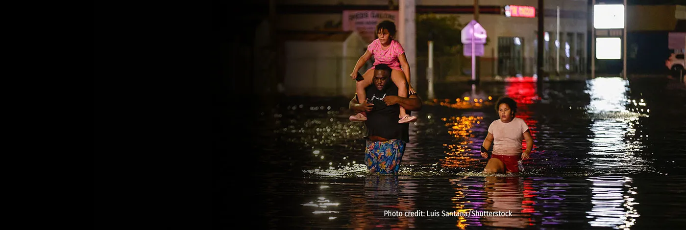 A man and two children wade through flooded water.