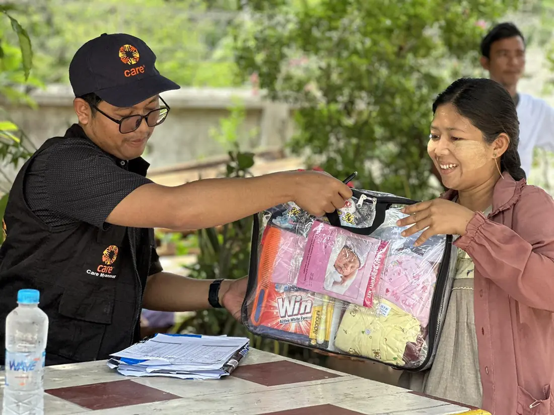 A CARE staff member hands a kit filled with baby supplies to a woman.