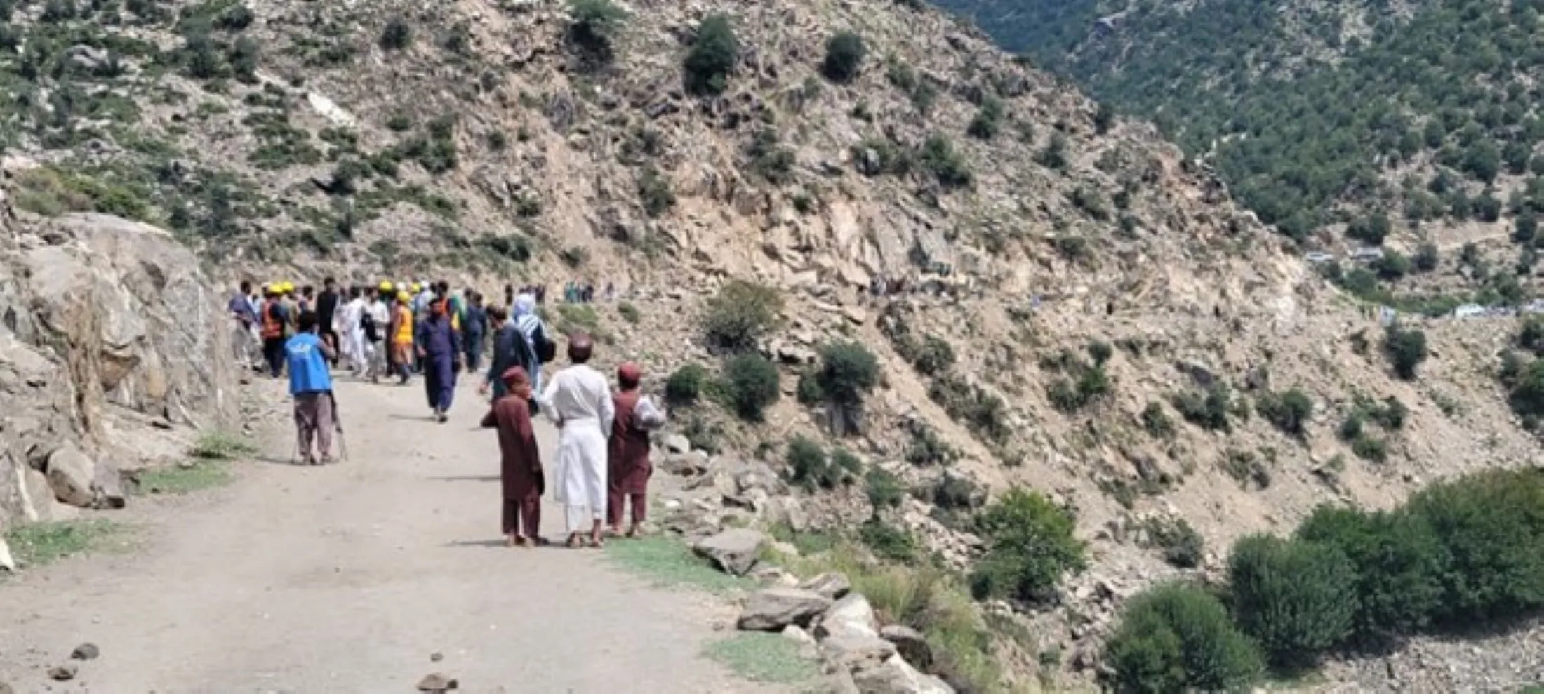 Group of Afghan residents gathered on mountain road assessing earthquake damage in remote mountainous region.