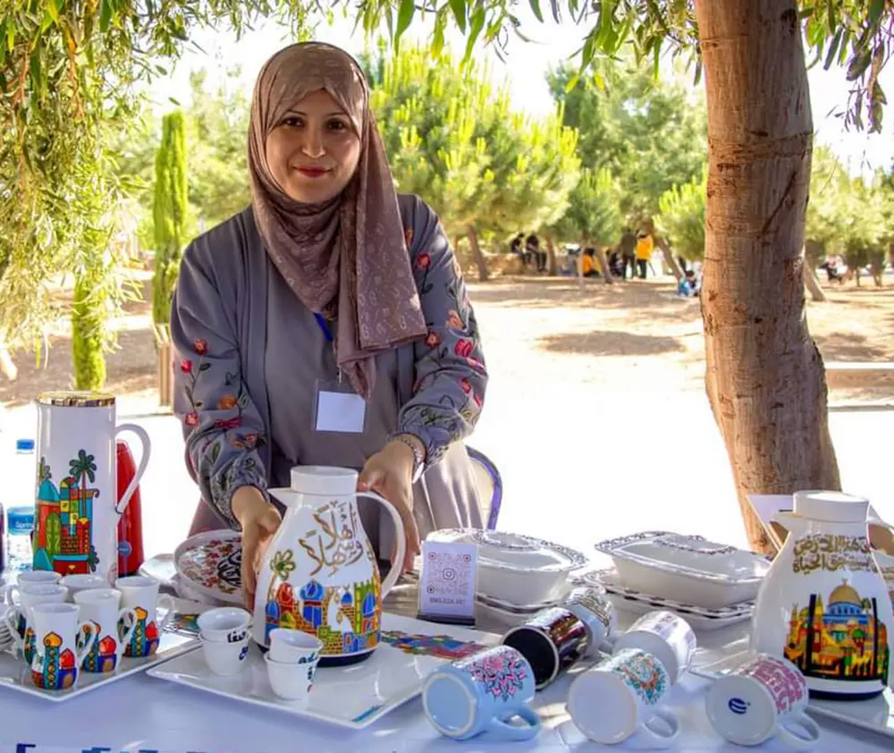 A Jordanian woman stands behind a table full of porcelain pitchers, mugs, bowls, and dishes.