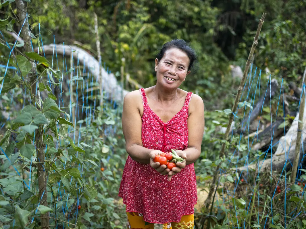 A Filipina woman holds a handful of tomatoes and okra.