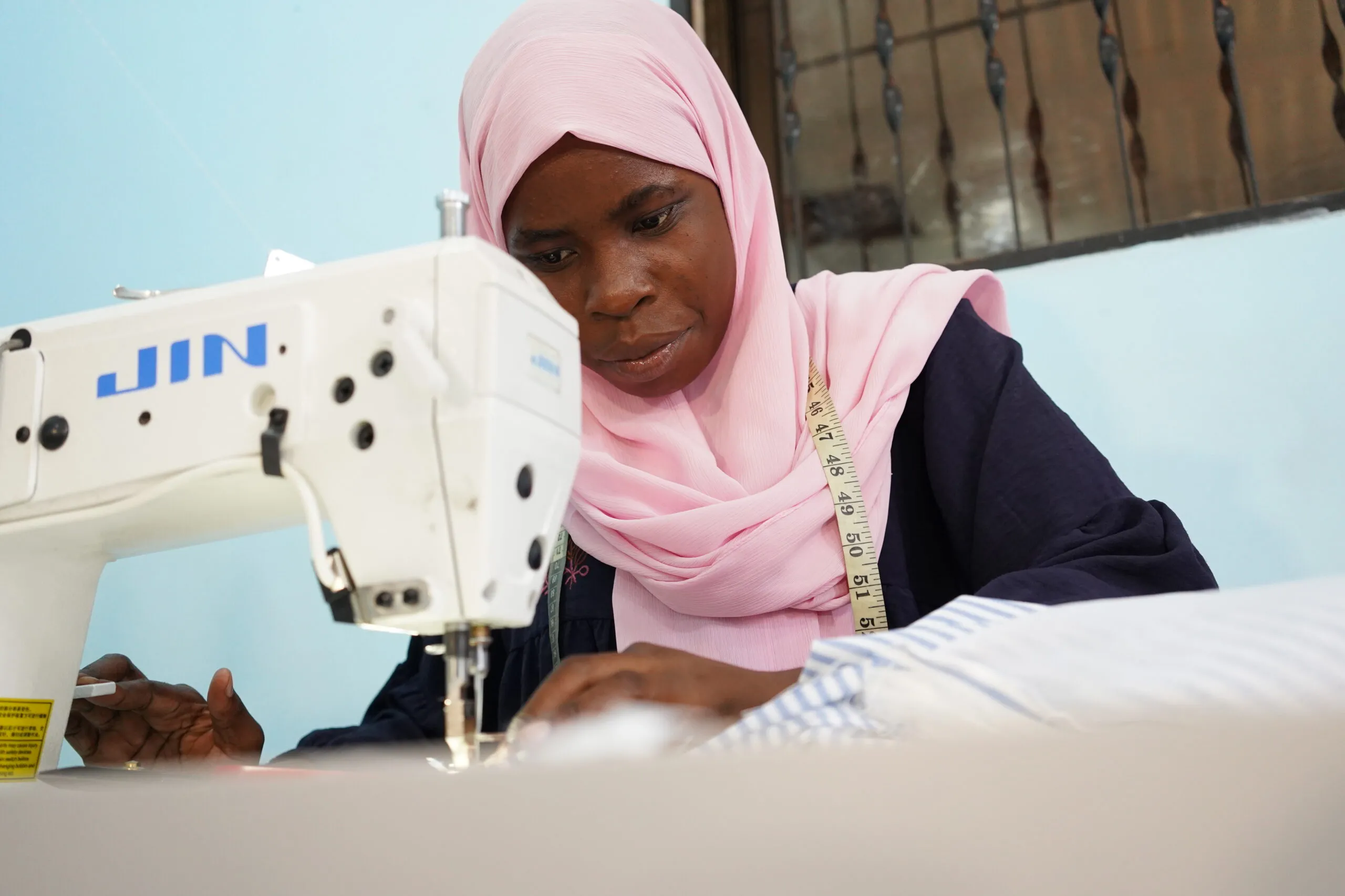 A woman in a pink headscarf leans over a sewing machine at the Arizona Vocational Center in Dar es Salaam, Tanzania.