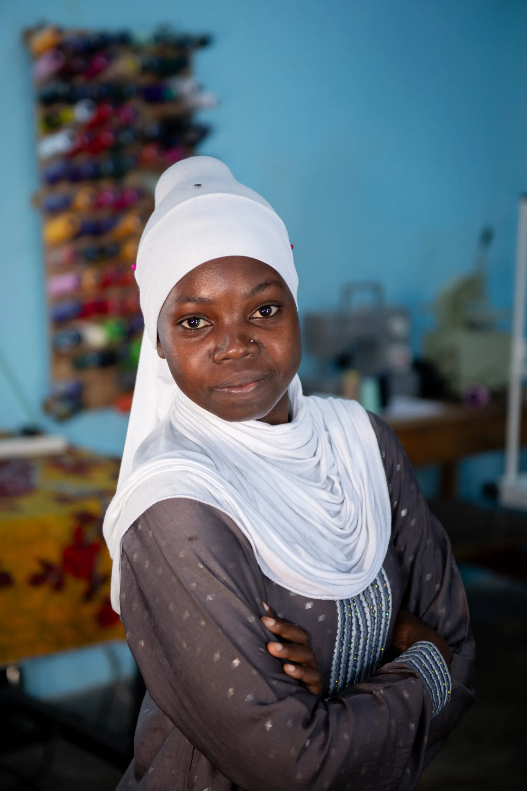 A young Tanzanian woman in a white headscarf looks at the camera with crossed arms.