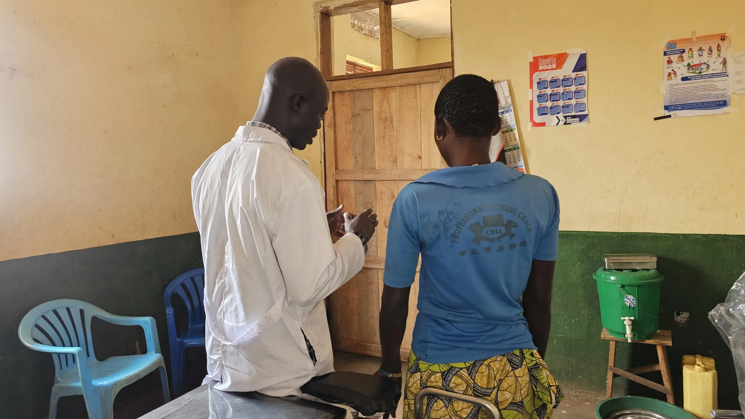 Two people stand with their backs to the camera at a rural healthcare clinic in DRC.