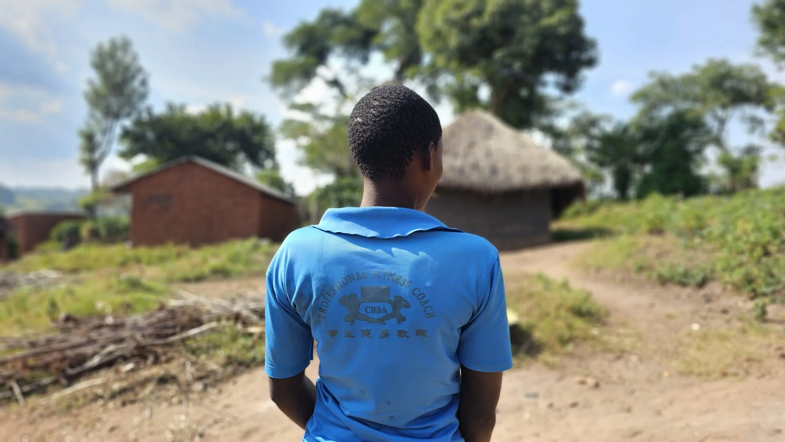 A young Congolese woman stands with her back to the camera in a rural village.
