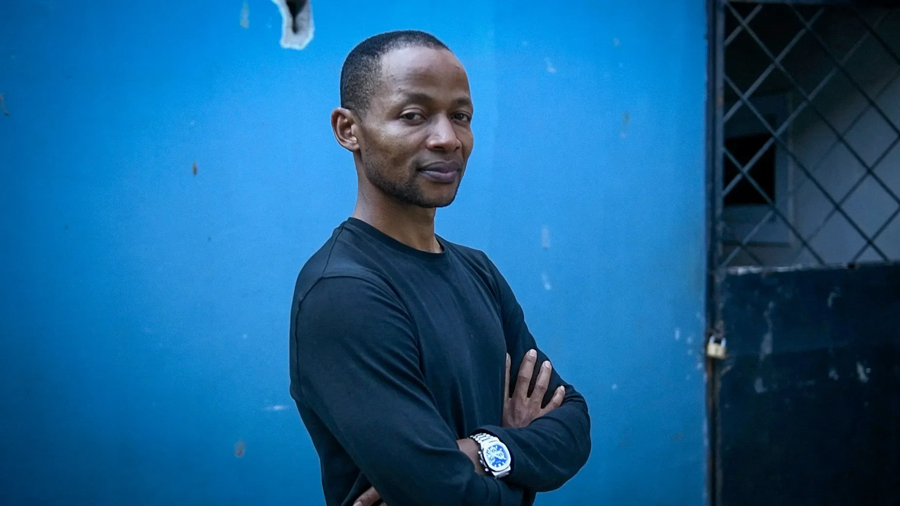 A Tanzanian man looks at the camera with crossed arms.