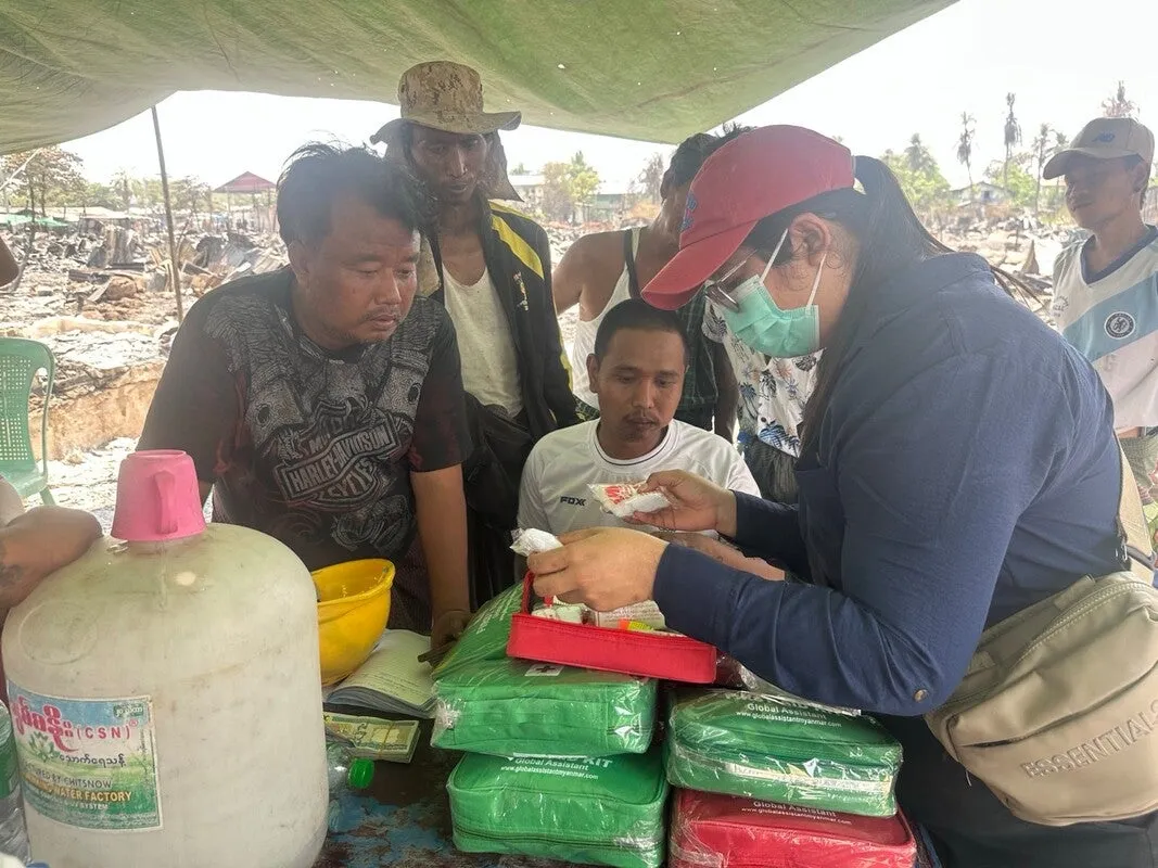 A woman wearing a facemask sorts through materials while a small group watches.