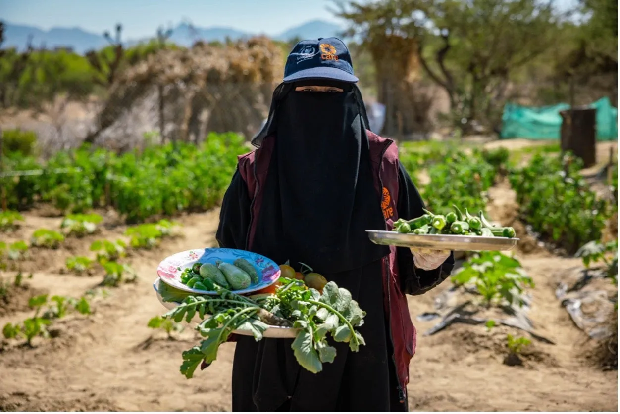 A veiled woman in a CARE hat and vest shows off the harvest from her garden in Yemen.