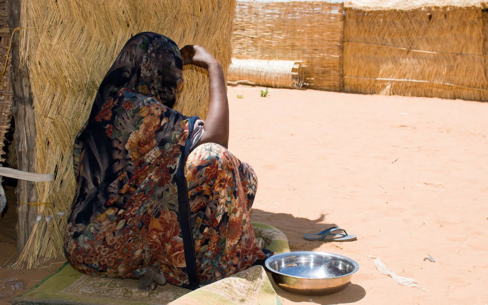 Woman sitting sideways near an emergency food center — known in Sudan as a community kitchen — with an empty pot beside her.