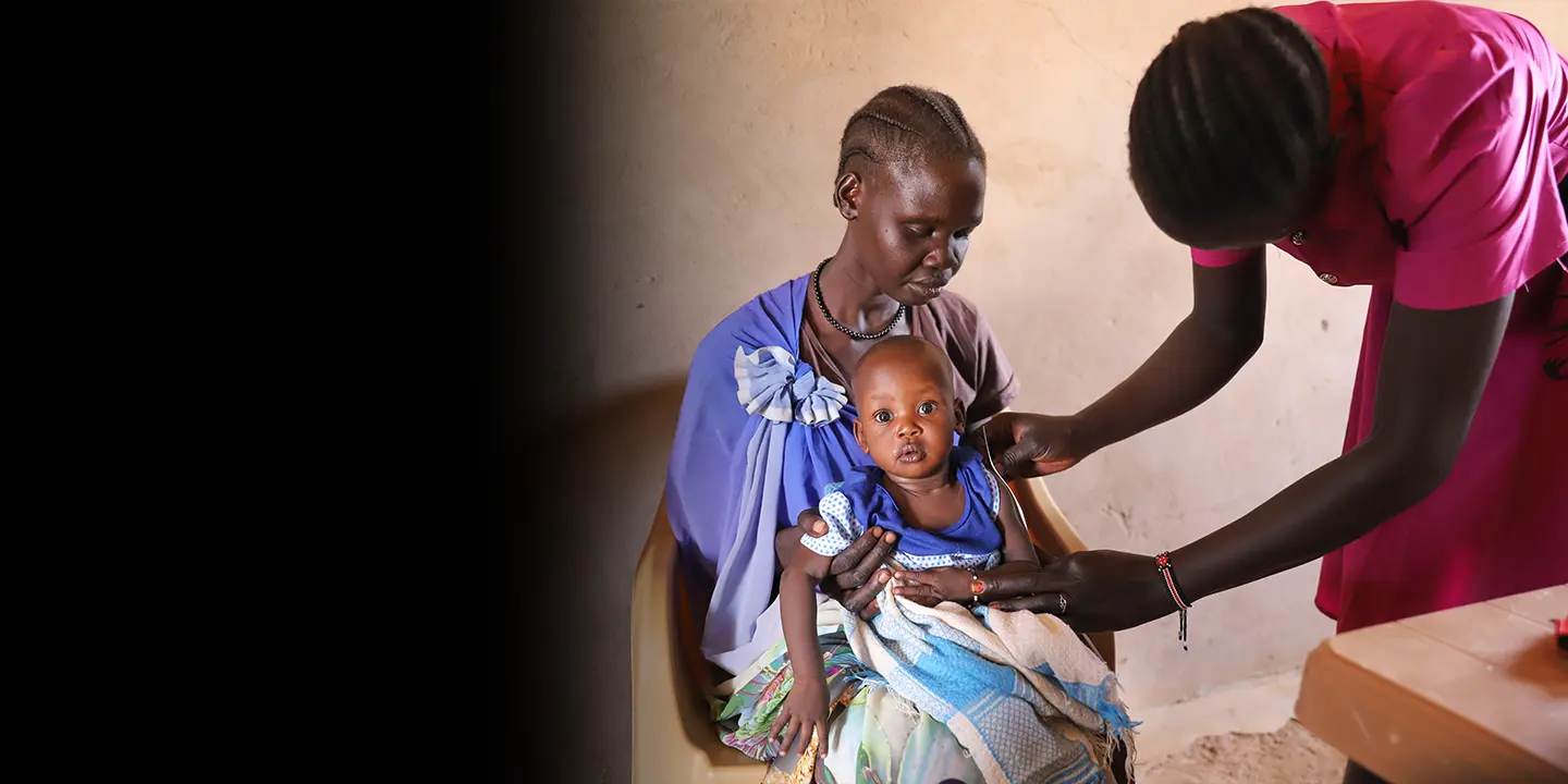 A nurse checks a child sitting on a woman's lap.