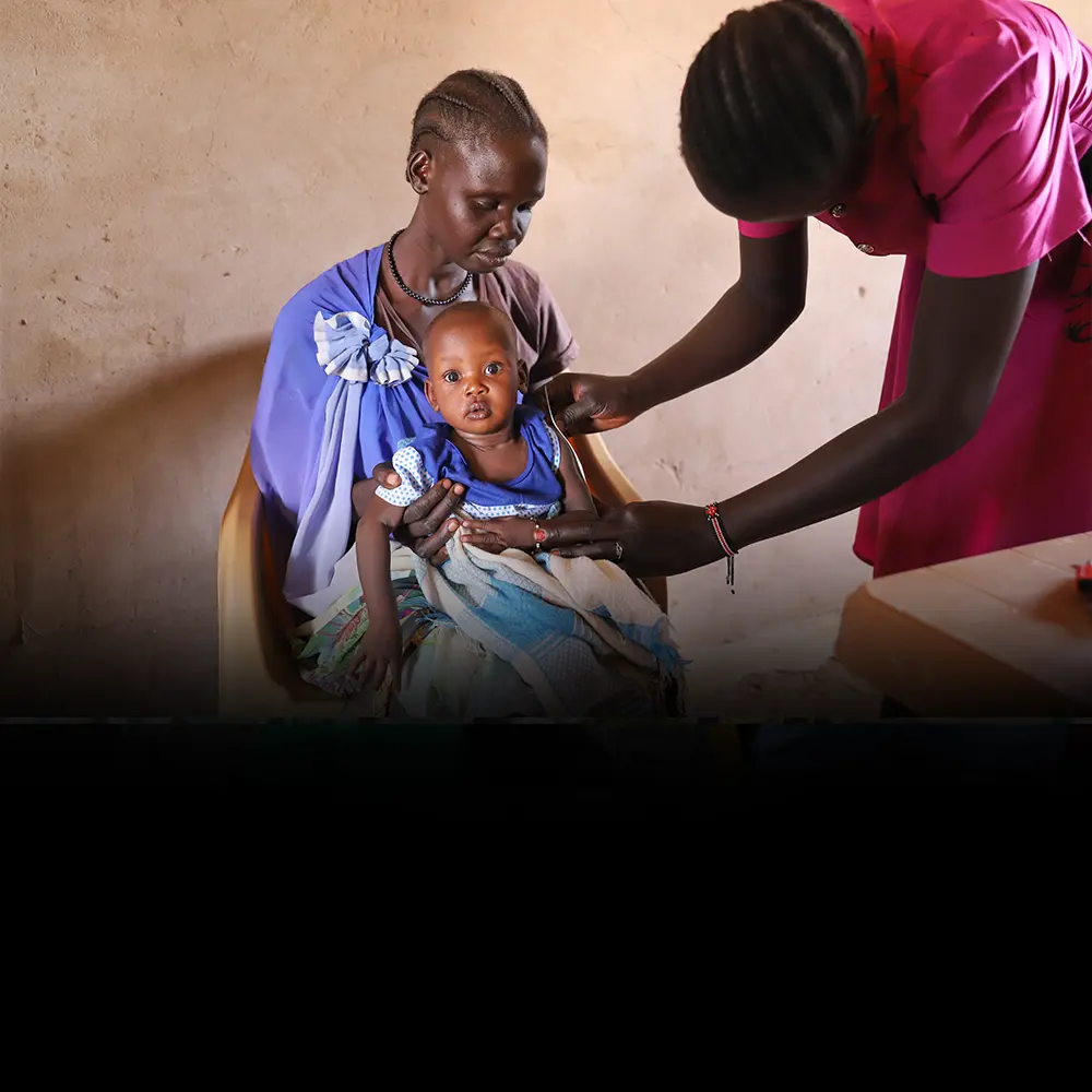 A nurse checks a child sitting on a woman's lap.