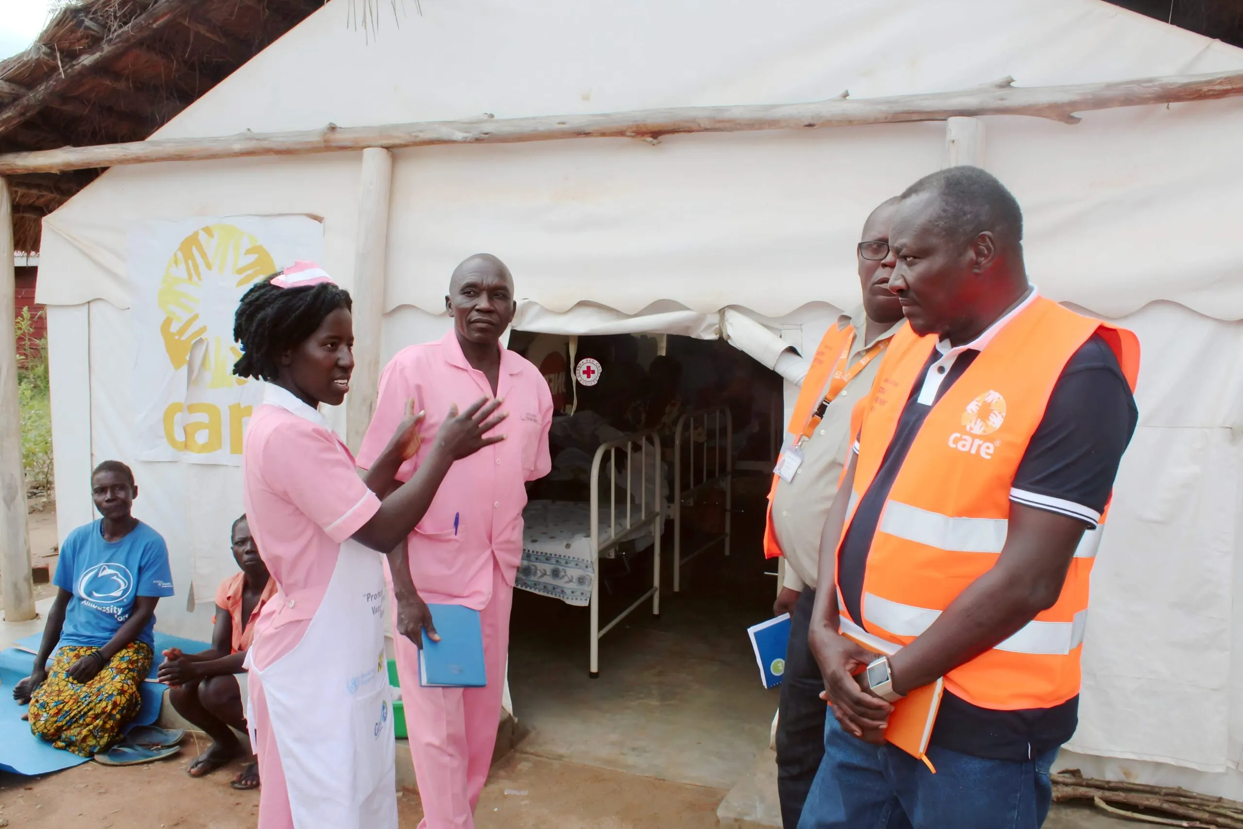 A man stands inside a health center, speaking with staff in a refugee settlement.