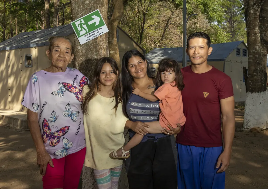 An intergenerational family of five stands together outside, smiling at the camera.