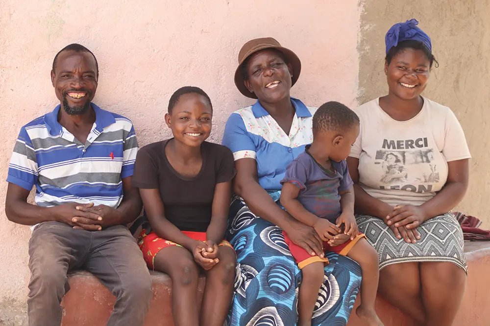 A family of five smiles while sitting on a bench.