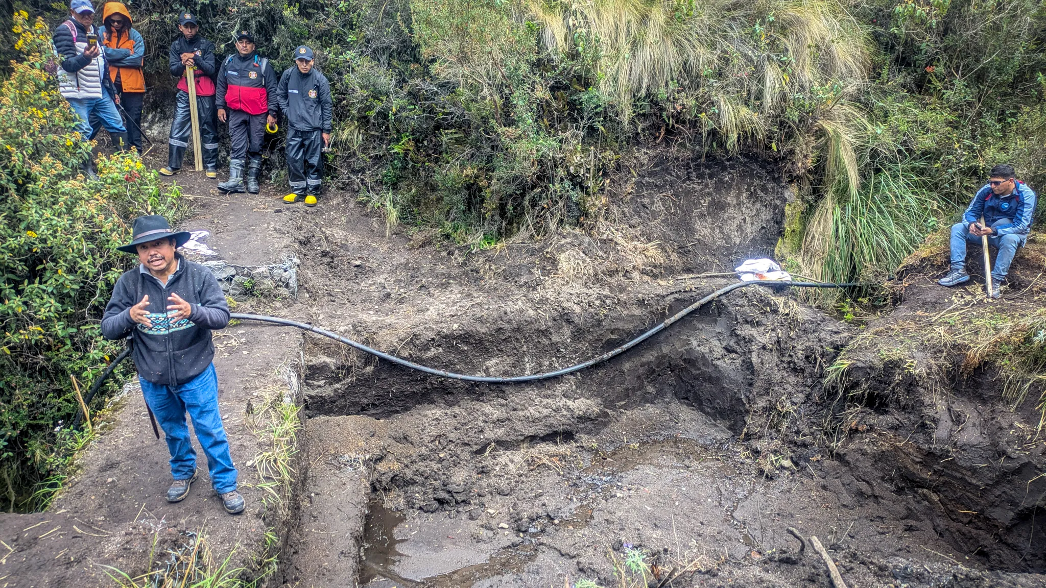 Hilario Morocho stands beside a large cut water reservoir, speaking to a group of firefighters and volunteers during a community work day.