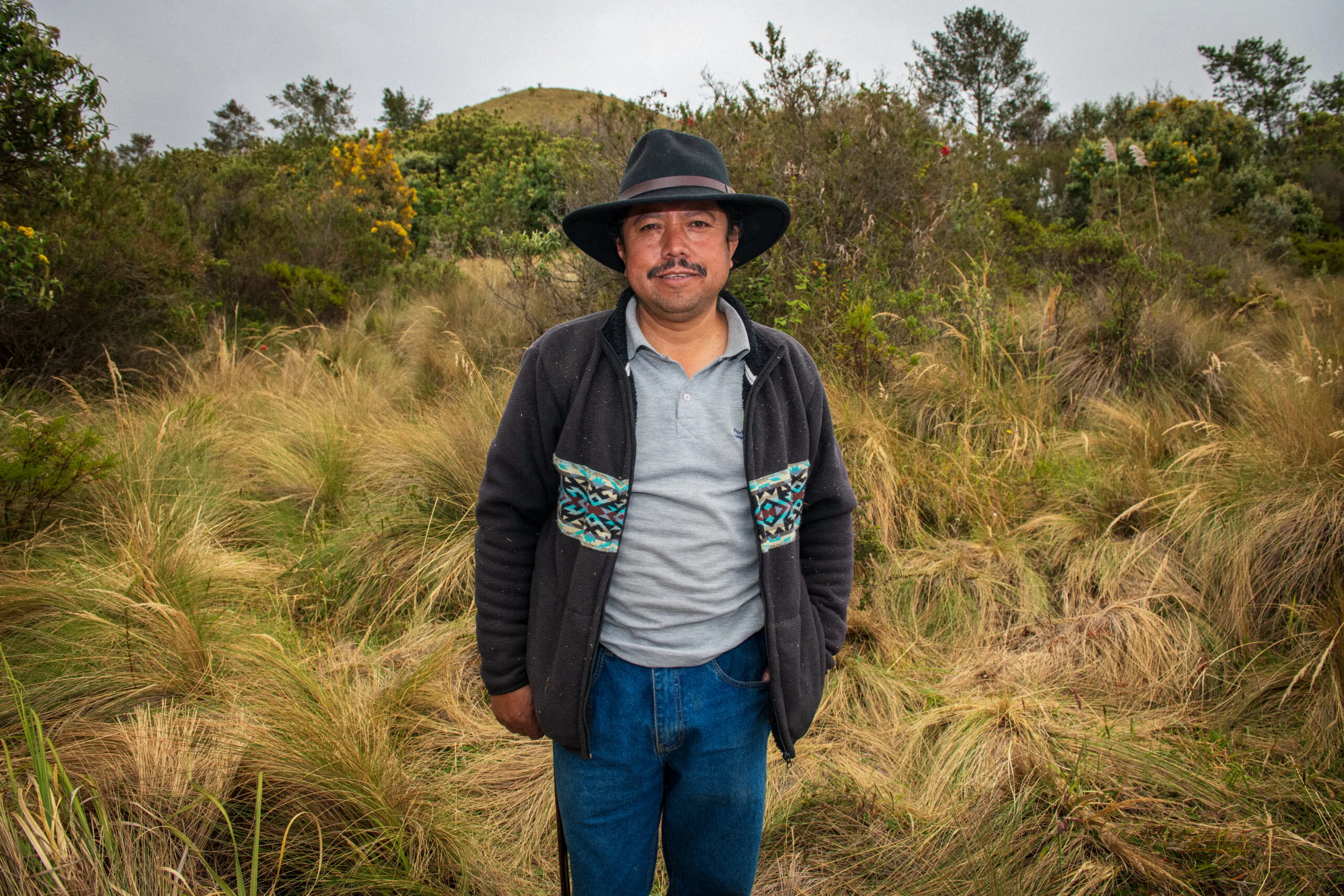 Portrait of Hilario Morocho wearing a wide-brimmed hat and jeans while standing in the páramo grasslands of Ecuador’s Andes.