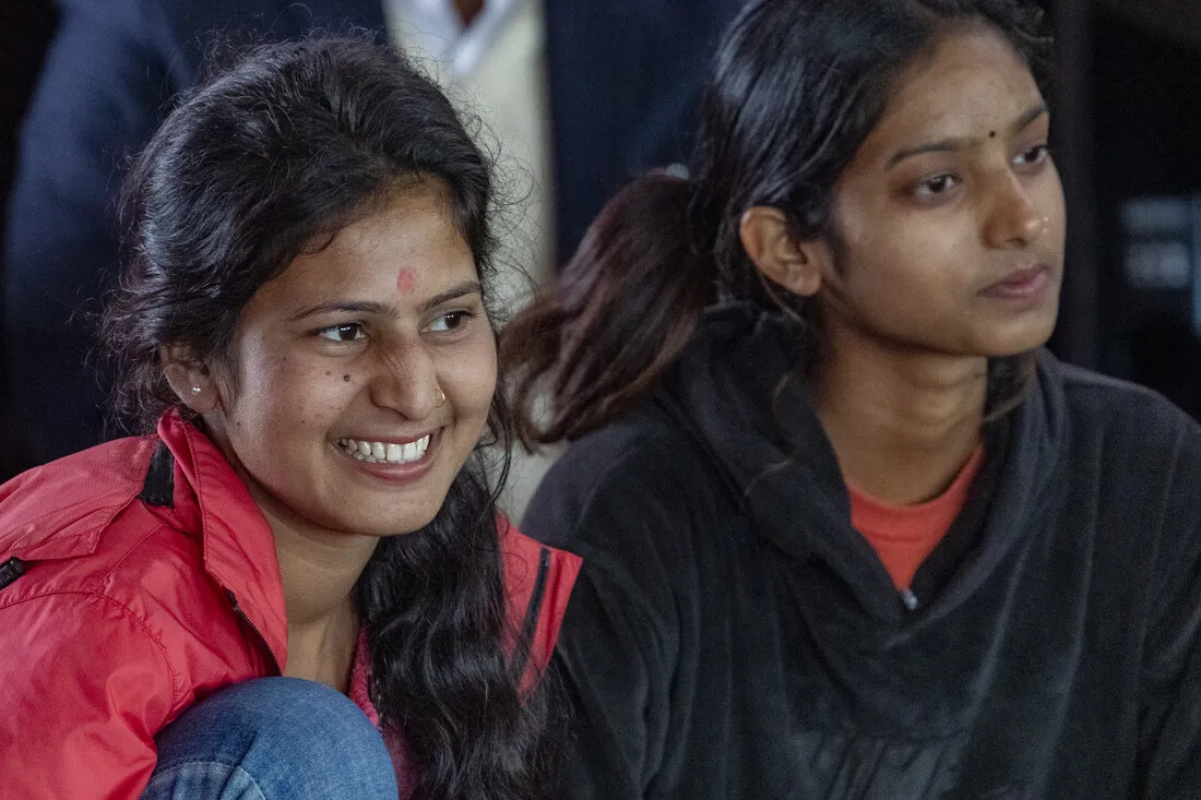 Two Nepali girls sit together and smile while listening to a speaker.
